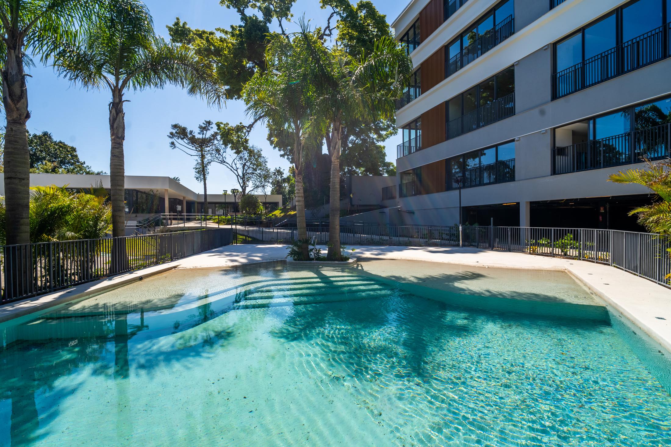Piscina do Aria com prainha, entre palmeiras, com o edifício ao fundo